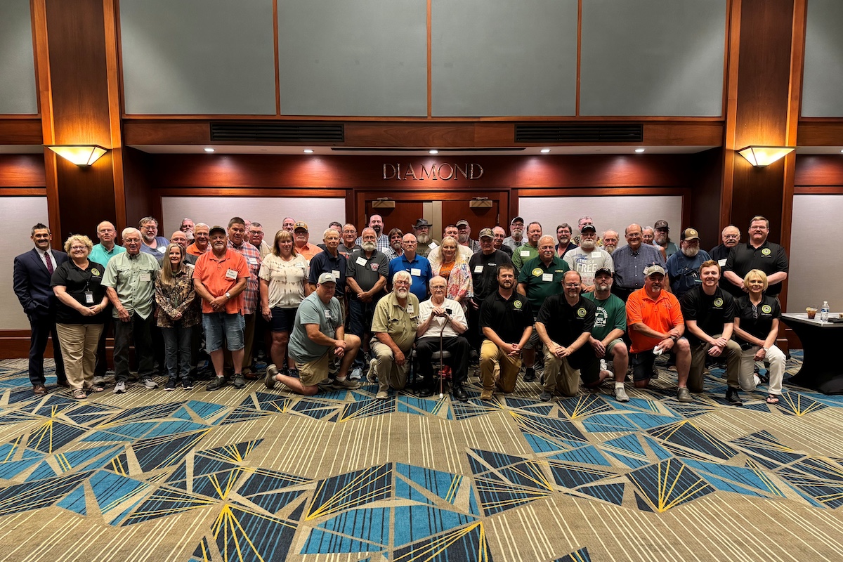 A group of people pose together in front of a conference room doorway. There three rows of people standing and one row kneeling.