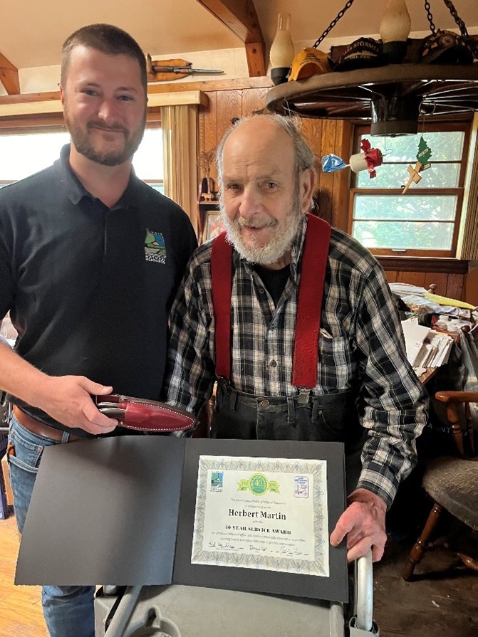 A younger man and an elderly man pose together as the elderly man accepts an award.