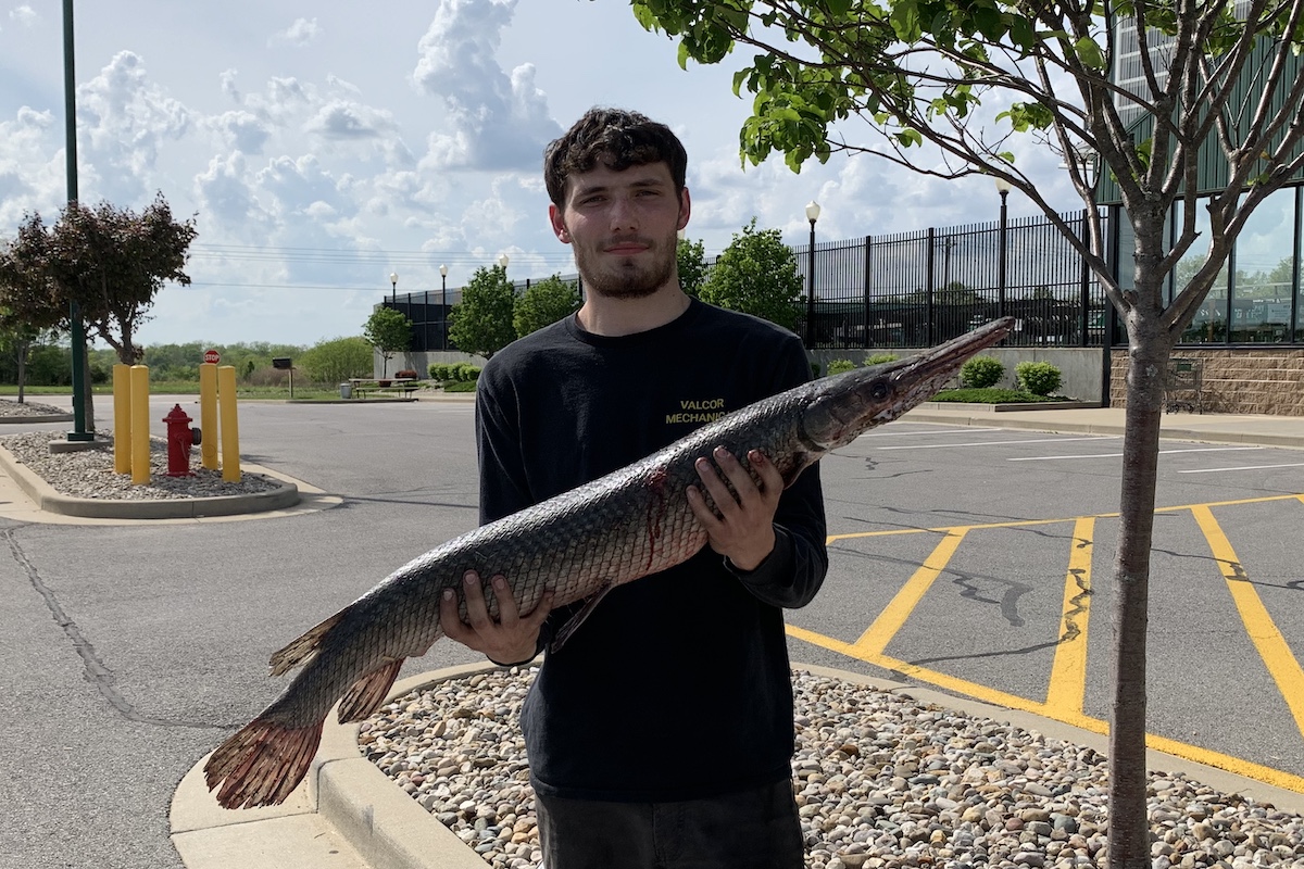 A man stands in a parking lot holding up with both hands a large fish.