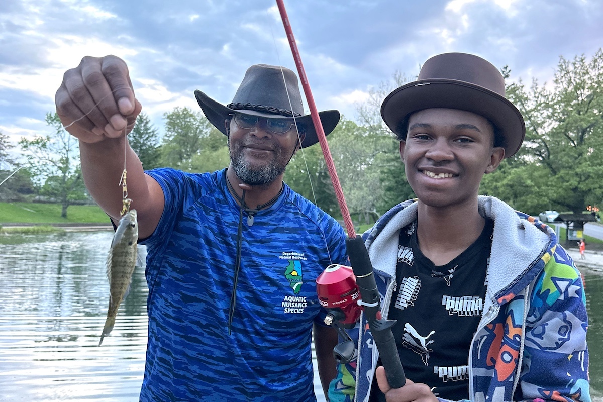 Eliha Perez, Representante de Educación para la Conservación del Departamento de Recursos Naturales de Illinois, posa con un estudiante y el pez que este capturó.