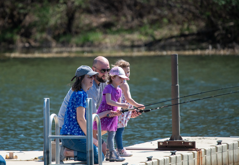 Two children with their mother and father fish while standing on a dock over a freshwater lake.