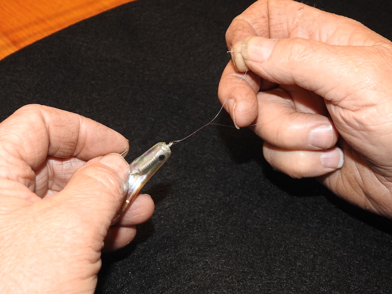 A close-up of a fisherman's hands as he ties a fishing lure on monofilament line.