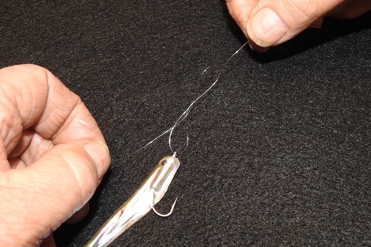A close-up of a fisherman's hands tying a fishing lure on to a fishing line.