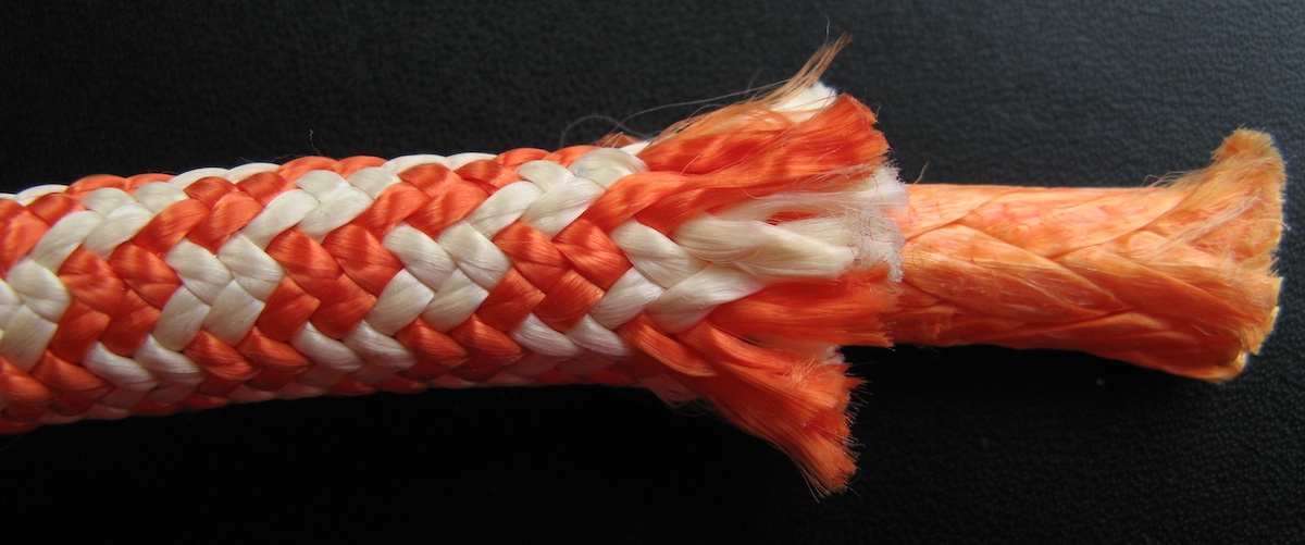 A close-up of an orange and white braided polyester rope frayed at one end to show the inner fibers.