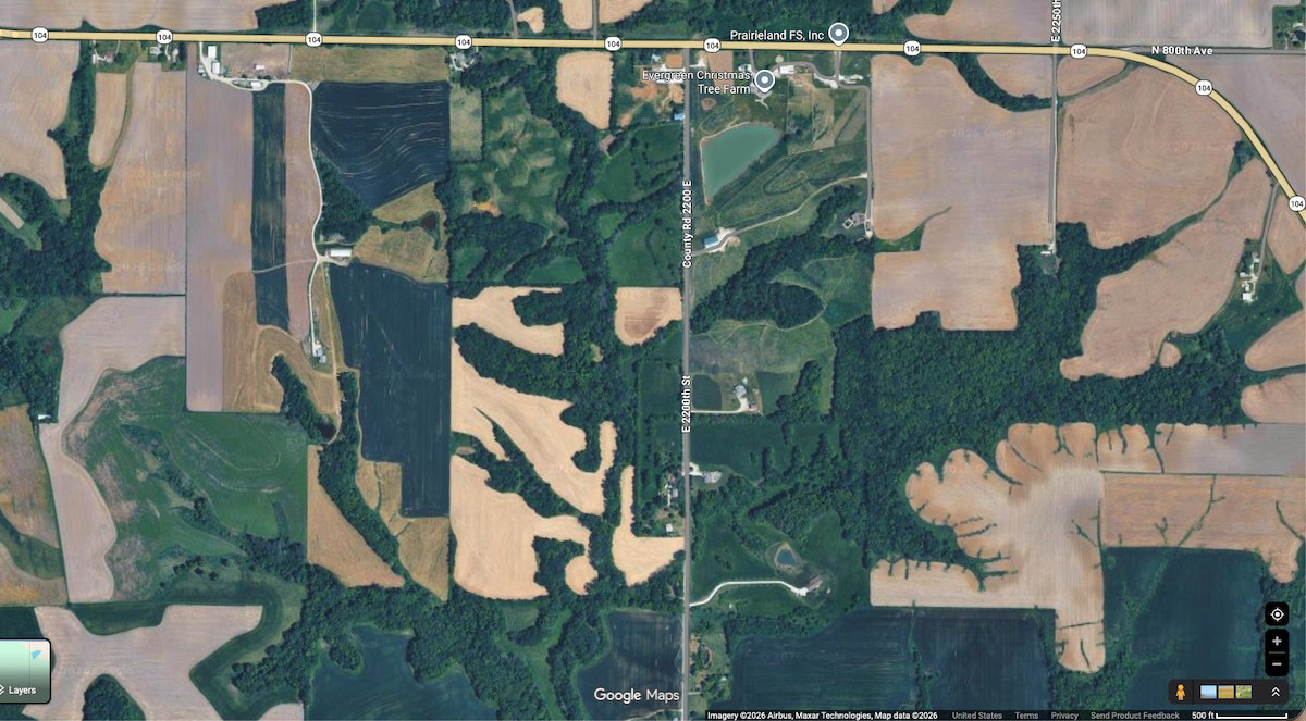 A aerial view of agricultural fields with grassy buffers between wooded ravines and forests.