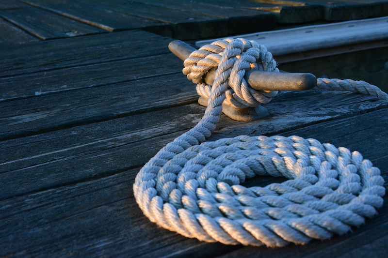 A close-up of rope used to tie a boat to a cleat on a wooden dock on a body of water..