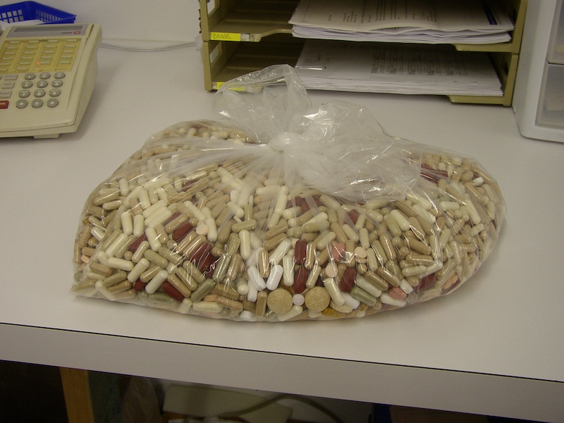 A sack of various capsules resting on a counter. In the background is a telephone to the left and a paperwork organizer to the right.
