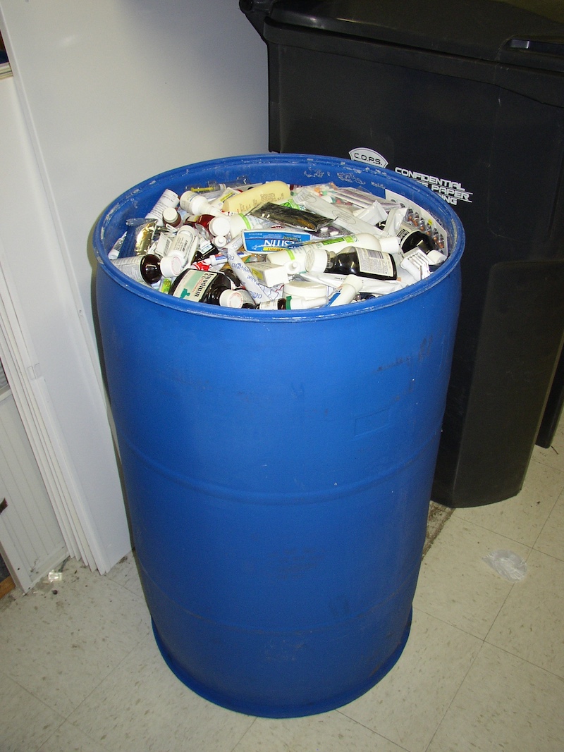 A blue plastic barrel filled with medicines, prescription pills, blister packs of capsules and nasal sprays.