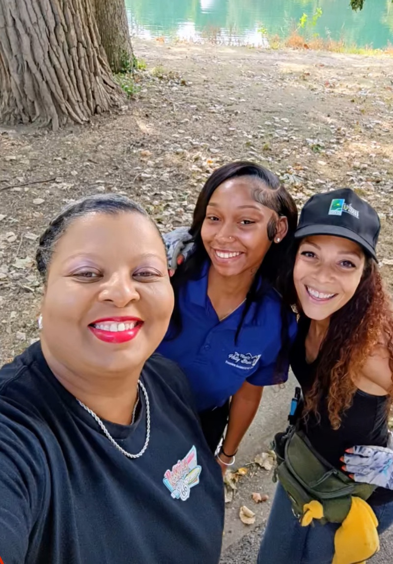 Three African American woman stand together. In the background is a dry fall shoreline next to a pond.