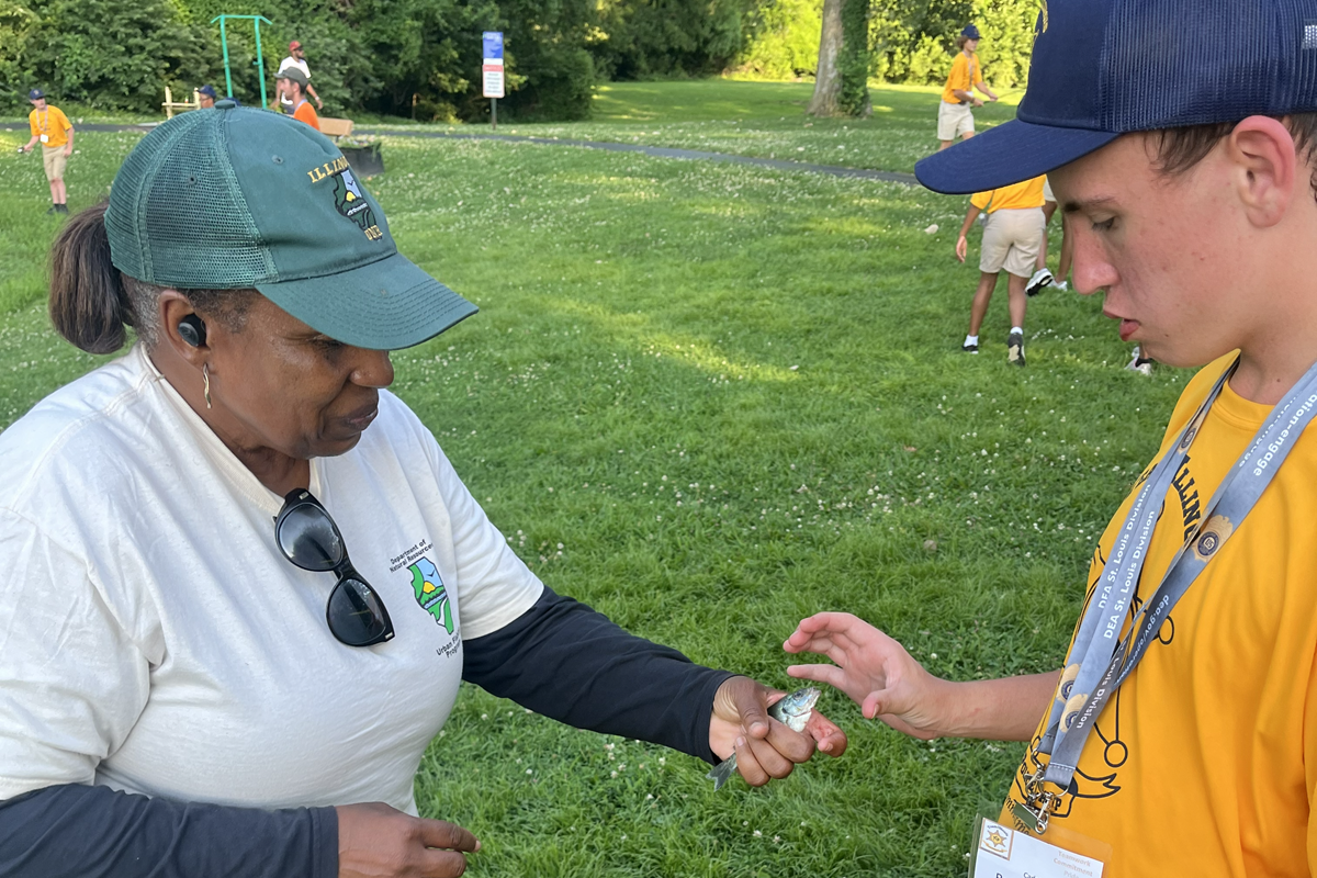 Illinois Department of Natural Resources Conservation Education Representative Dee Toombs hands a small fish to a teenage fishing camp participant.